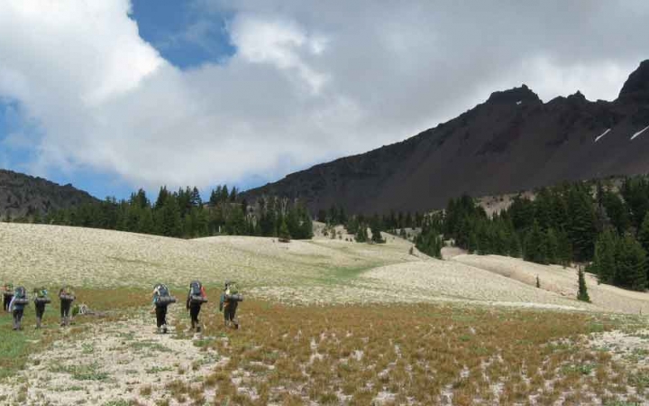 a group of students hike across an alpine meadow on an outward bound trip